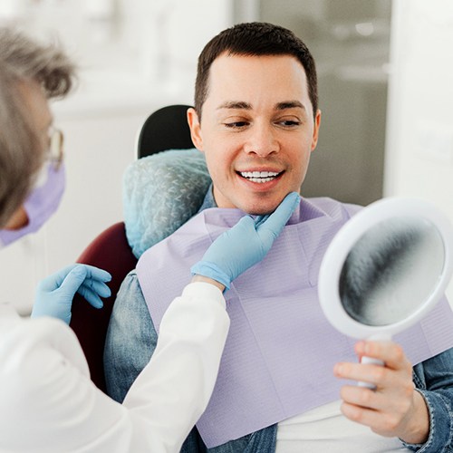 Man smiling at reflection in mirror with dentist