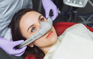 A woman with brown hair in red dental chair with nitrous oxide mask on nose