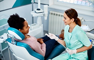 Woman in blue dental chair smiling and dentist in pale teal scrubs