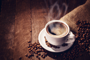 Steaming cup of coffee surrounded by coffee beans